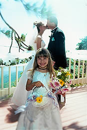 Flower girl in front of bride and groom kissing at their complete wedding.